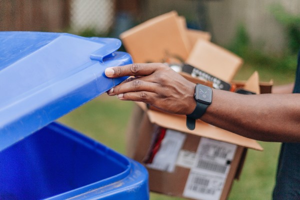 man's arm throwing arm throwing cardboard packaging into a blue recycling bin